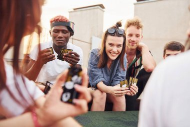 Masada oturup kağıt oynamak. Gündelik giysiler içinde bir grup genç gündüz vakti çatıda parti veriyor..