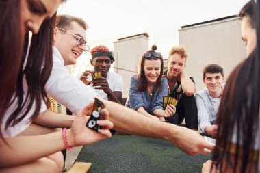 Masada oturup kağıt oynamak. Gündelik giysiler içinde bir grup genç gündüz vakti çatıda parti veriyor..