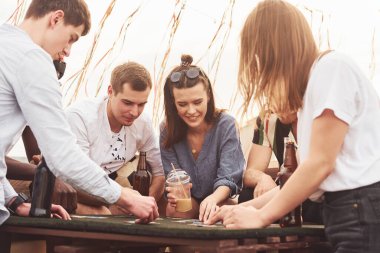 Oyun oynayıp masanın başında oturmak. Gündelik giysiler içinde bir grup genç gündüz vakti çatıda parti veriyor..