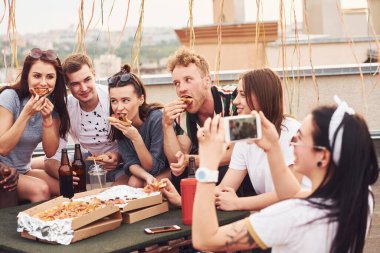 Fotoğraf çekiyorum. Lezzetli pizza. Gündelik giysiler içinde bir grup genç gündüz vakti çatıda parti veriyor..