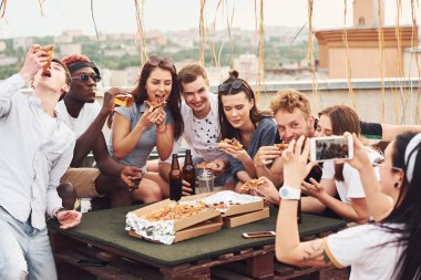Fotoğraf çekiyorum. Lezzetli pizza. Gündelik giysiler içinde bir grup genç gündüz vakti çatıda parti veriyor..