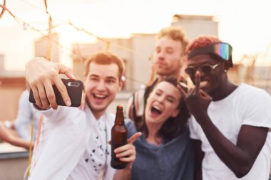 Birlikte durup selfie çekiyoruz. Gündelik giysiler içinde bir grup genç gündüz vakti çatıda parti veriyor..