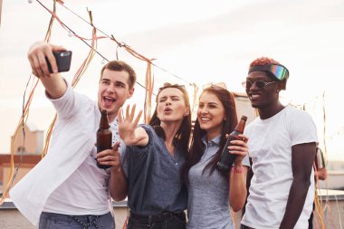 Birlikte durup selfie çekiyoruz. Gündelik giysiler içinde bir grup genç gündüz vakti çatıda parti veriyor..