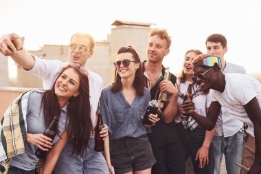 Telefonla selfie çekiyoruz. Gündelik giysiler içinde bir grup genç gündüz vakti çatıda parti veriyor..