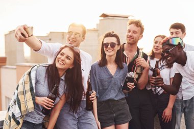 Telefonla selfie çekiyoruz. Gündelik giysiler içinde bir grup genç gündüz vakti çatıda parti veriyor..