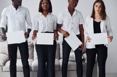 Resmi giyinmiş bir grup Afrikalı Amerikalı ofiste koltuğun yanında el ele tutuşup boş kağıtları tutuyorlar..