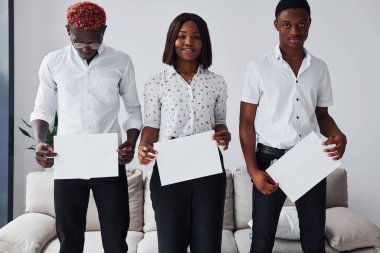 Resmi giyinmiş bir grup Afrikalı Amerikalı ofiste koltuğun yanında el ele tutuşup boş kağıtları tutuyorlar..