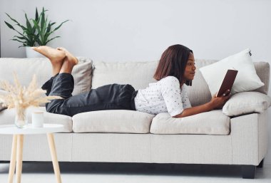 Ellerinde not defteriyle kanepeye uzanmış beyaz gömlekli Afro-Amerikan kadın..