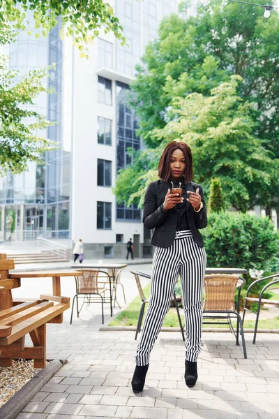 Telefonu bekletiyorum. Şehirde, yeşil ağaçların yanında ve iş inşaatına karşı şık giyinmiş Afro-Amerikalı genç bir kadın..