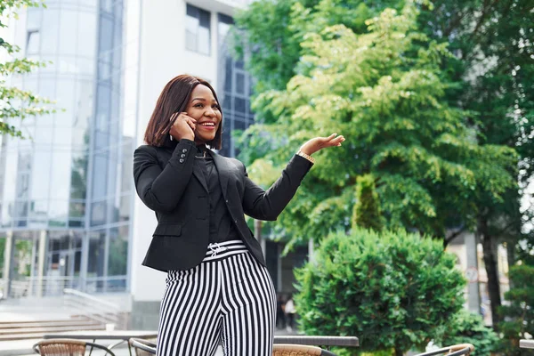 Telefonla konuşuyorum. Şehirde, yeşil ağaçların yanında ve iş inşaatına karşı şık giyinmiş Afro-Amerikalı genç bir kadın..