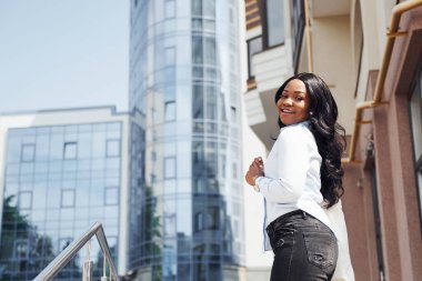 Beyaz gömlekli genç Afro-Amerikan kadın şehir dışında iş binasına karşı..