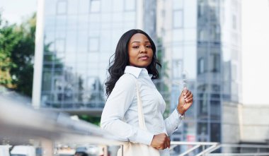 Beyaz gömlekli genç Afro-Amerikan kadın şehir dışında iş binasına karşı..