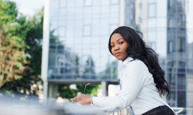 Beyaz gömlekli genç Afro-Amerikan kadın şehir dışında iş binasına karşı..
