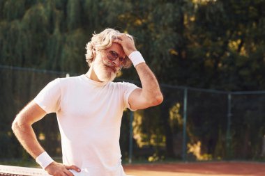 Gözlüklü, beyaz gömlekli ve tenis kortunda siyah şortlu son sınıf stil sahibi bir adam..