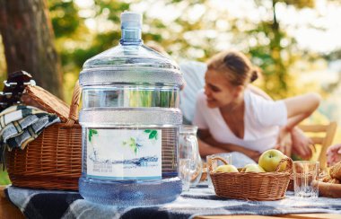 Masada büyük plastik bir su şişesi var. Bir grup gencin dışarıda, ormanda tatili var. Hafta sonu ve arkadaşlık kavramı.