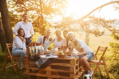 Piknik masasında oturuyor. Bir grup gencin dışarıda, ormanda tatili var. Hafta sonu ve arkadaşlık kavramı.