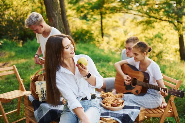 Woman eats apple. Group of young people have vacation outdoors in the forest. Conception of weekend and friendship.