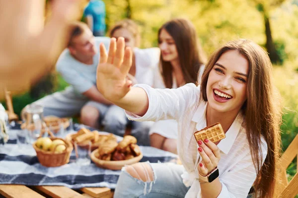 Woman giving high five to photographer. Group of young people have vacation outdoors in the forest. Conception of weekend and friendship.