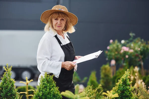 Not defteri elimde. Kıdemli kadın gündüz vakti bahçede olur. Bitki ve mevsim kavramı.