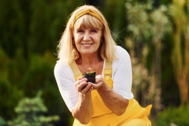 İş günü. Sarı üniformalı. Kıdemli kadın gündüz vakti bahçede olur. Bitki ve mevsim kavramı.