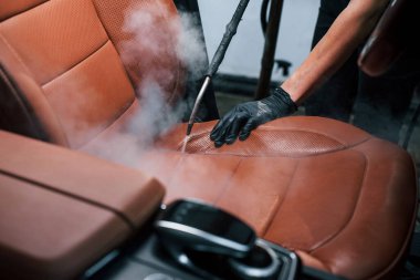 Buhar temizleyicisi kullanıyor. Modern siyah otomobil, araba yıkama istasyonunda bir kadın tarafından hizmet vermektedir..