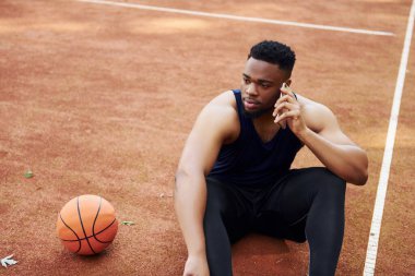 Telefonla konuşuyor. Afrikalı Amerikalı adam dışarıda basketbol oynuyor..