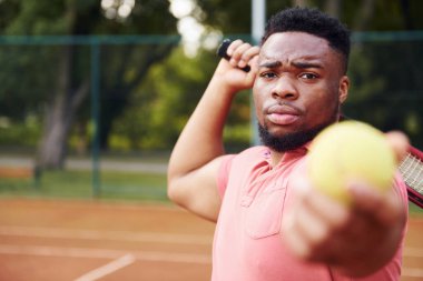Pembe tişörtlü Afro-Amerikan adam dışarıda tenis oynuyor..