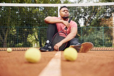 Ağa yakın oturuyor ve mola veriyor. Pembe tişörtlü Afro-Amerikan bir adam tenis raketiyle dışarıda oturuyor..
