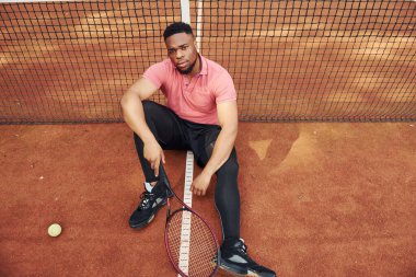 Ağa yakın oturuyor ve mola veriyor. Pembe tişörtlü Afro-Amerikan bir adam tenis raketiyle dışarıda oturuyor..