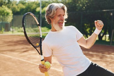 Zaferi kutluyoruz. Gündüz vakti tenis kortunda raketi olan son sınıf modern stil sahibi bir adam..