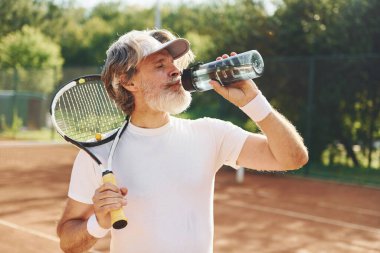 Mola verip su içiyorum. Gündüz vakti tenis kortunda raketi olan son sınıf modern stil sahibi bir adam..