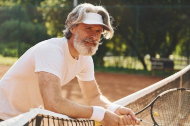 Gündüz vakti tenis kortunda raketi olan son sınıf modern stil sahibi bir adam..