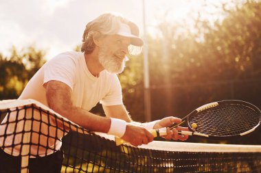 Gündüz vakti tenis kortunda raketi olan son sınıf modern stil sahibi bir adam..
