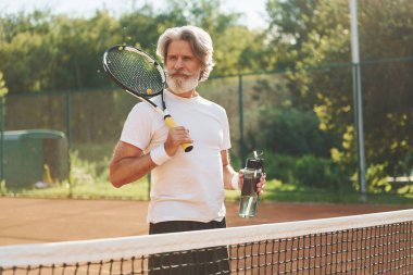 Raket tutuyor. Gündüz vakti tenis kortunda raketi olan son sınıf modern stil sahibi bir adam..