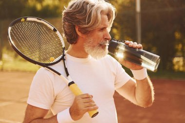 Mola verip su içiyorum. Gündüz vakti tenis kortunda raketi olan son sınıf modern stil sahibi bir adam..