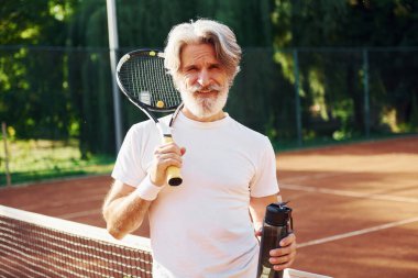 Bir şişe su tutuyorum. Gündüz vakti tenis kortunda raketi olan son sınıf modern stil sahibi bir adam..