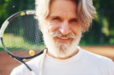 Raket tutuyor. Gündüz vakti tenis kortunda raketi olan son sınıf modern stil sahibi bir adam..