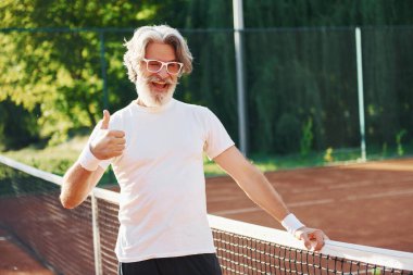 Kamera için poz vermek. Güneş gözlüklü. Son sınıf modern stil adamı gündüz vakti spor sahasında..