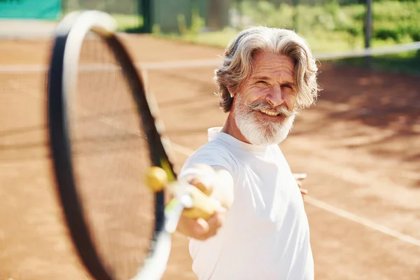 Playing game. Senior modern stylish man with racket outdoors on tennis court at daytime.