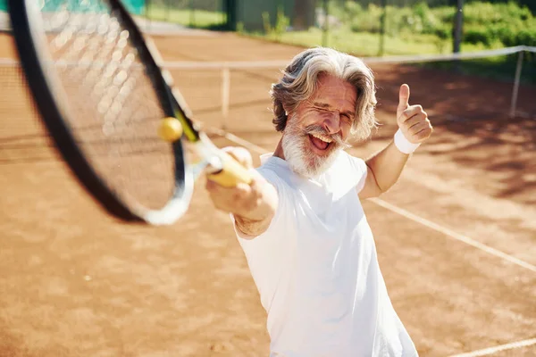 Playing game. Senior modern stylish man with racket outdoors on tennis court at daytime.