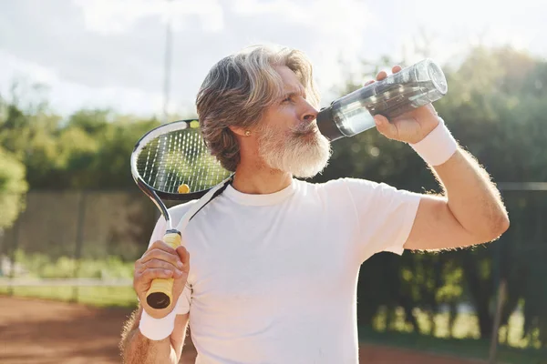 Mola verip su içiyorum. Gündüz vakti tenis kortunda raketi olan son sınıf modern stil sahibi bir adam..