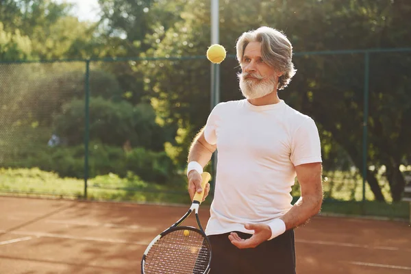 Training time. Senior modern stylish man with racket outdoors on tennis court at daytime.