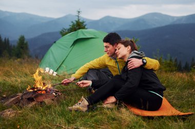 Kamp ateşinin yanında lokum yemiş bir çift. Majestic Karpat Dağları. Dokunulmamış doğanın güzel manzarası.