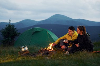 Klasik marşmelov kamp ateşinin yanında yapılıyor. Genç bir çift. Majestic Karpat Dağları. Dokunulmamış doğanın güzel manzarası.