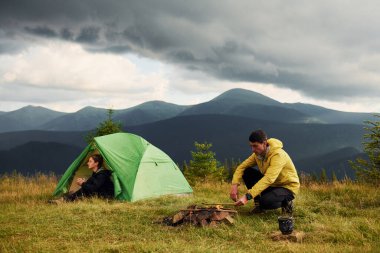 Kamp ateşi yakan adam. Kız arkadaşı daha yeni uyandı. Majestic Karpat Dağları. Dokunulmamış doğanın güzel manzarası.