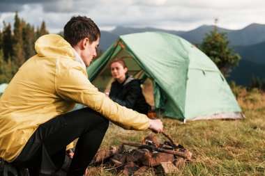 Kamp ateşi yakan adam. Kız arkadaşı daha yeni uyandı. Majestic Karpat Dağları. Dokunulmamış doğanın güzel manzarası.