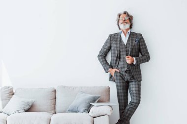 Zarif kıyafetler içinde. Beyaz duvara yaslanmış. Gri saçlı ve sakallı son sınıf modacı modern adam..