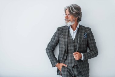 Zarif kıyafetler içinde. Beyaz duvara yaslanmış. Gri saçlı ve sakallı son sınıf modacı modern adam..