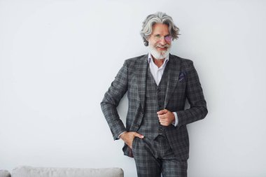 Zarif kıyafetler içinde. Beyaz duvara yaslanmış. Gri saçlı ve sakallı son sınıf modacı modern adam..