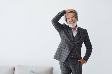 Zarif kıyafetler içinde. Beyaz duvara yaslanmış. Gri saçlı ve sakallı son sınıf modacı modern adam..